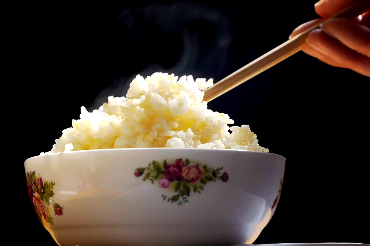 prikaz kuvanog pirinča i osobe koja ga uzima sa drvenim štapićima